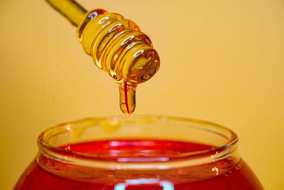Honig tropft von Honiglöffel in ein Glas mit Honig