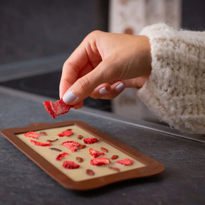 Weiße Tafelschokolade wir mit Erdbeeren von einer Frauenhand dekoriert